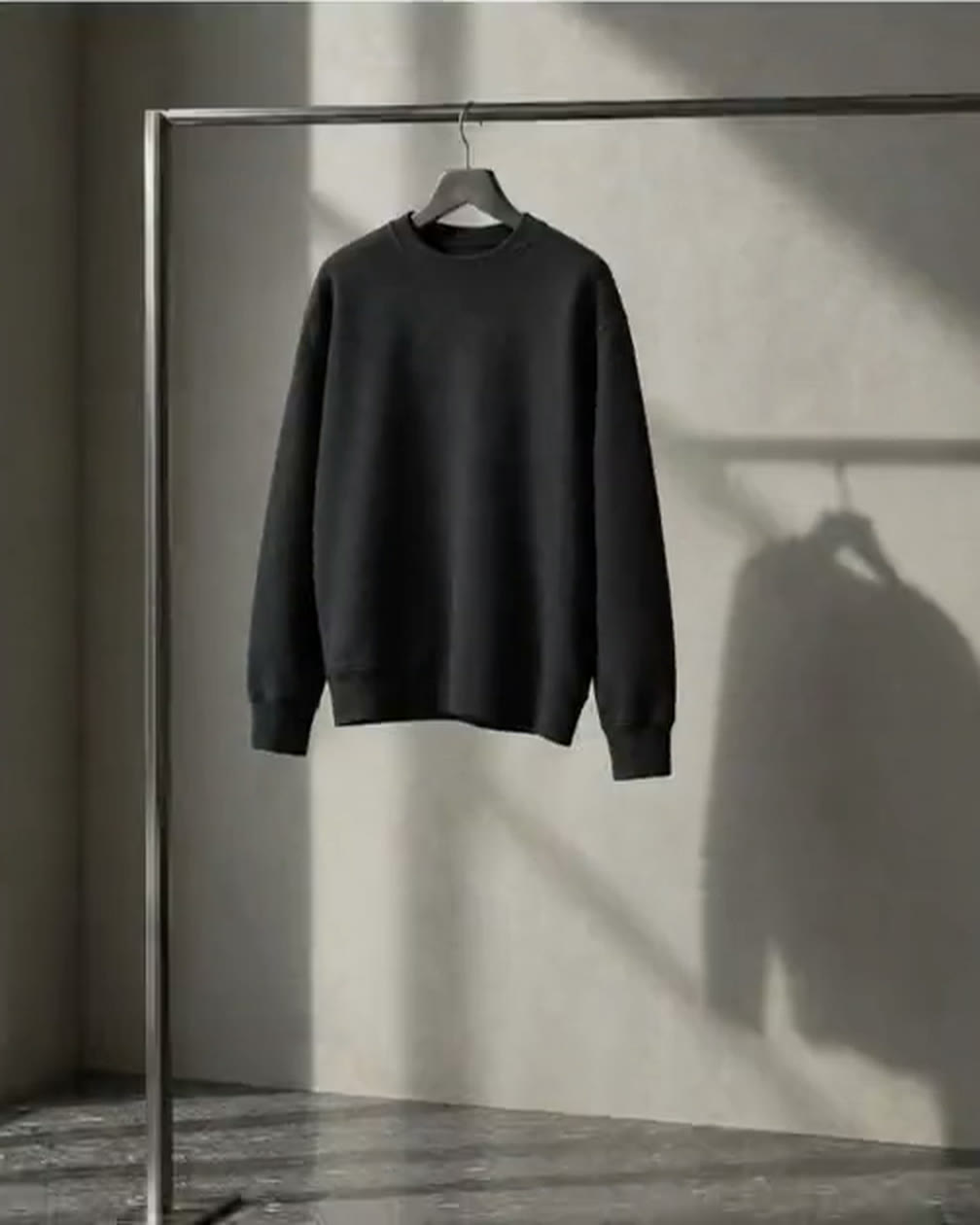 A black crewneck on a steel rail in raking window light, from the Bedrock Basics storefront.